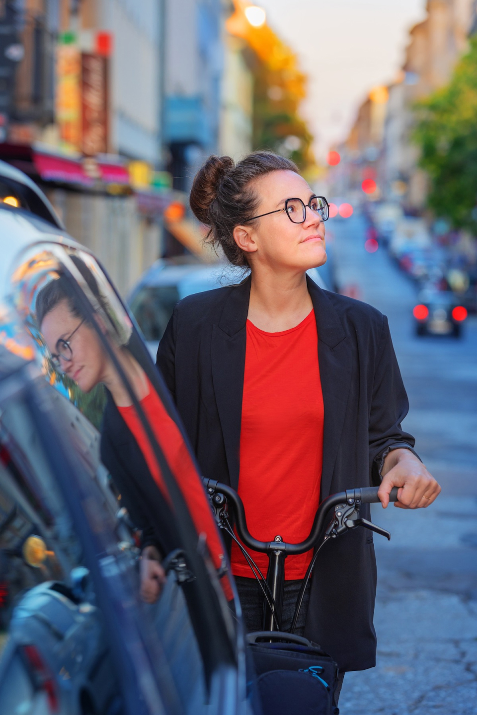 Katja Diehl steht mit Fahrrad am Straßenrand zwischen parkenden Autos, blickt seitlich nach oben