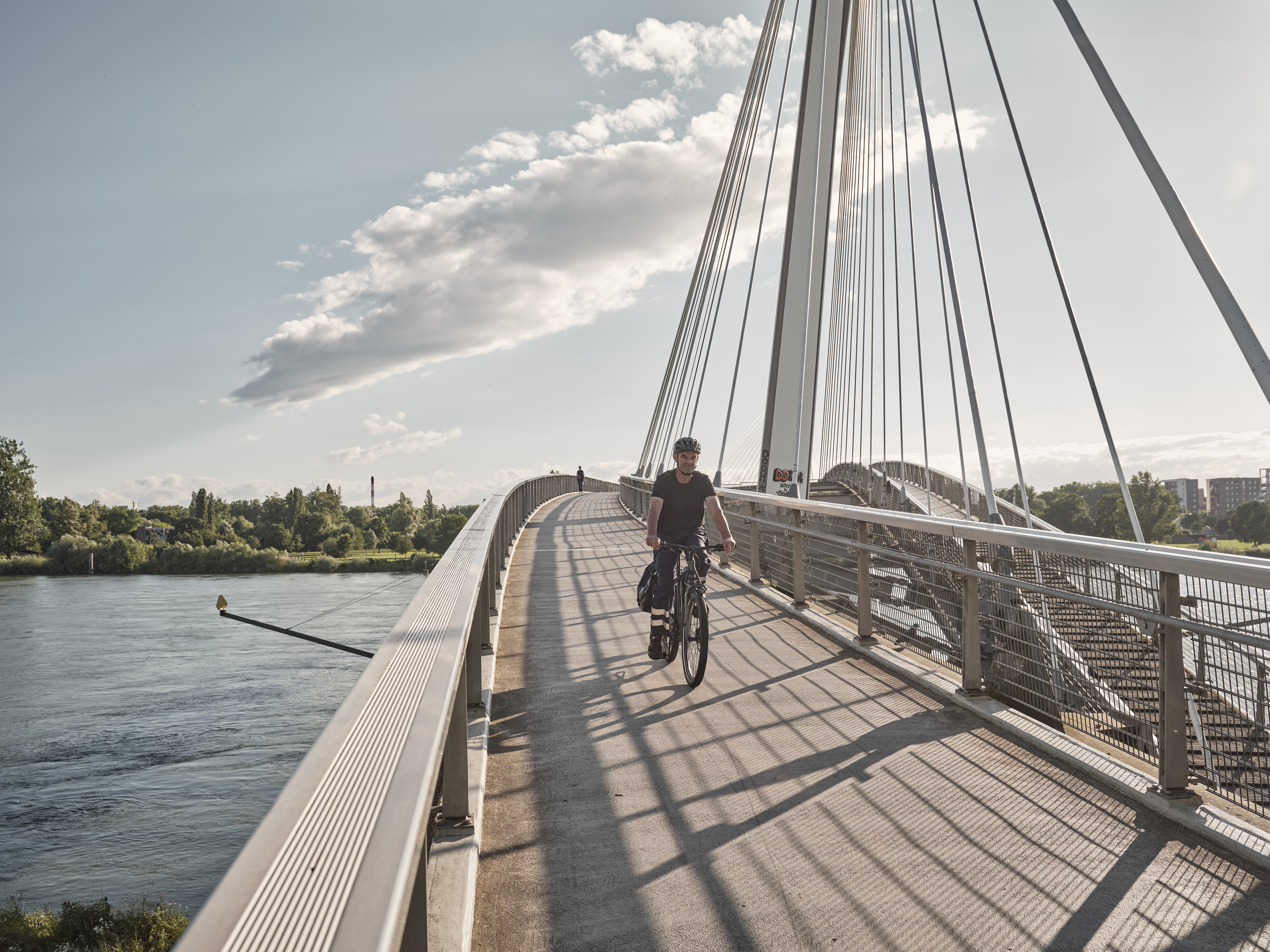 Radfahrer in Arbeitskleidung auf Fahrradbrücke über Fluss